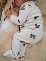 baby dressed in cream footed sleepsuit with holly & candy cane sleeping with candy cane in hand