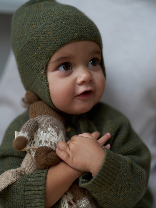 baby in forest moss green wool tassel hat with chin tie & matching cardigan hugging wool toys