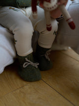 baby in forest moss green wool booties with grey ribbons & cream leggings with olive prints