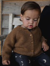 baby dressed in black salopette with cream moons & chestnut brown wool cardigan