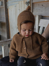 baby wearing brown wool hat with tassel & chin tie with cardigan & black leggings with moon print