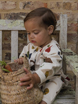 baby wearing long-sleeve onesie with fresh produce print grabbing straw basket with carrots