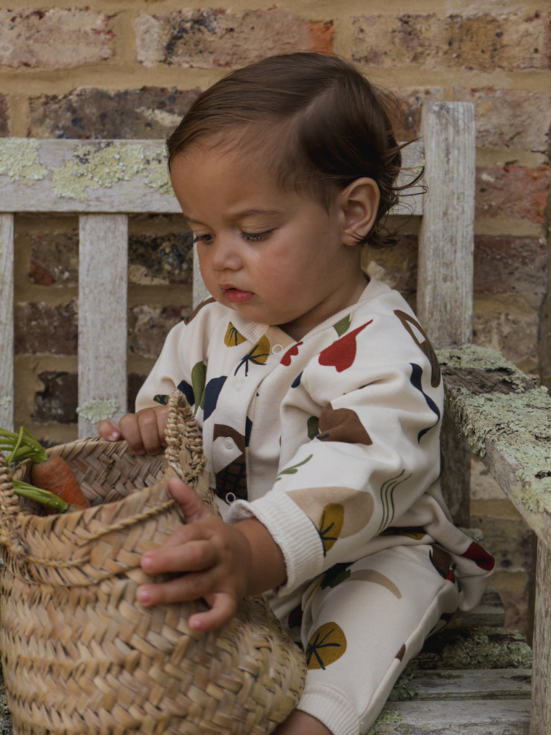 baby wearing long-sleeve onesie with fresh produce print grabbing straw basket with carrots