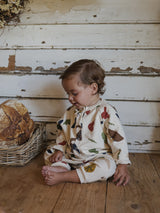 baby dressed in cream long-sleeve onesie with fresh farm produce print sitting beside bread basket