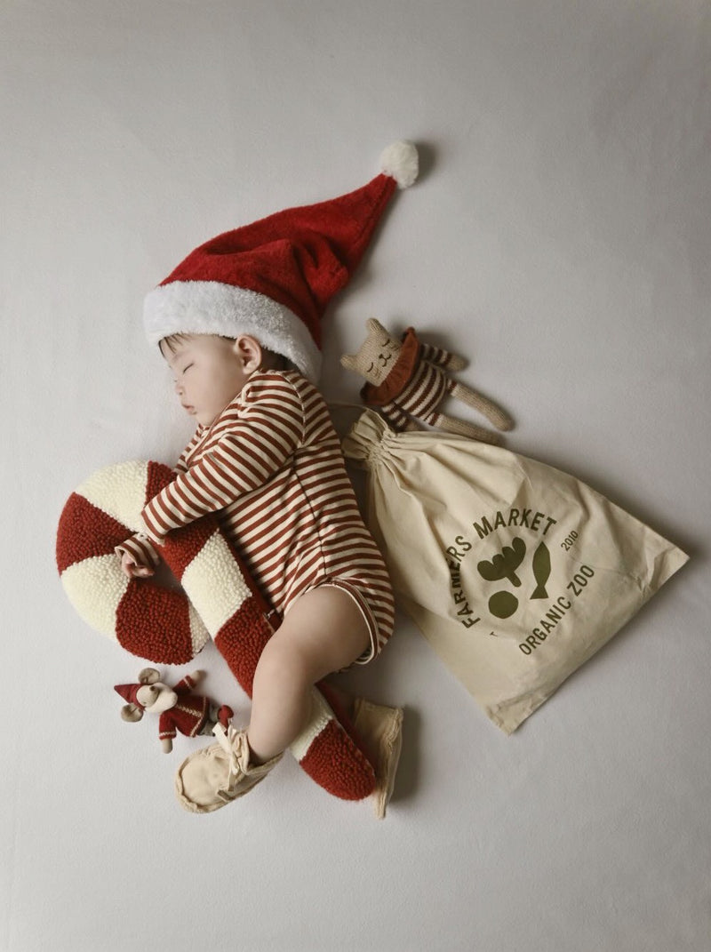 flat lay of baby in red white stripes bodysuit cream booties santa hat hugging candy cane with drawstring bag