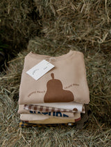 folded baby & toddler autumn apparel in brown cream & yellow stacked together on straw bale