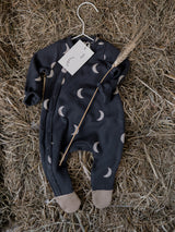 baby & toddler footed suit in black with cream moons on hanger on top of straw with wheat stalk