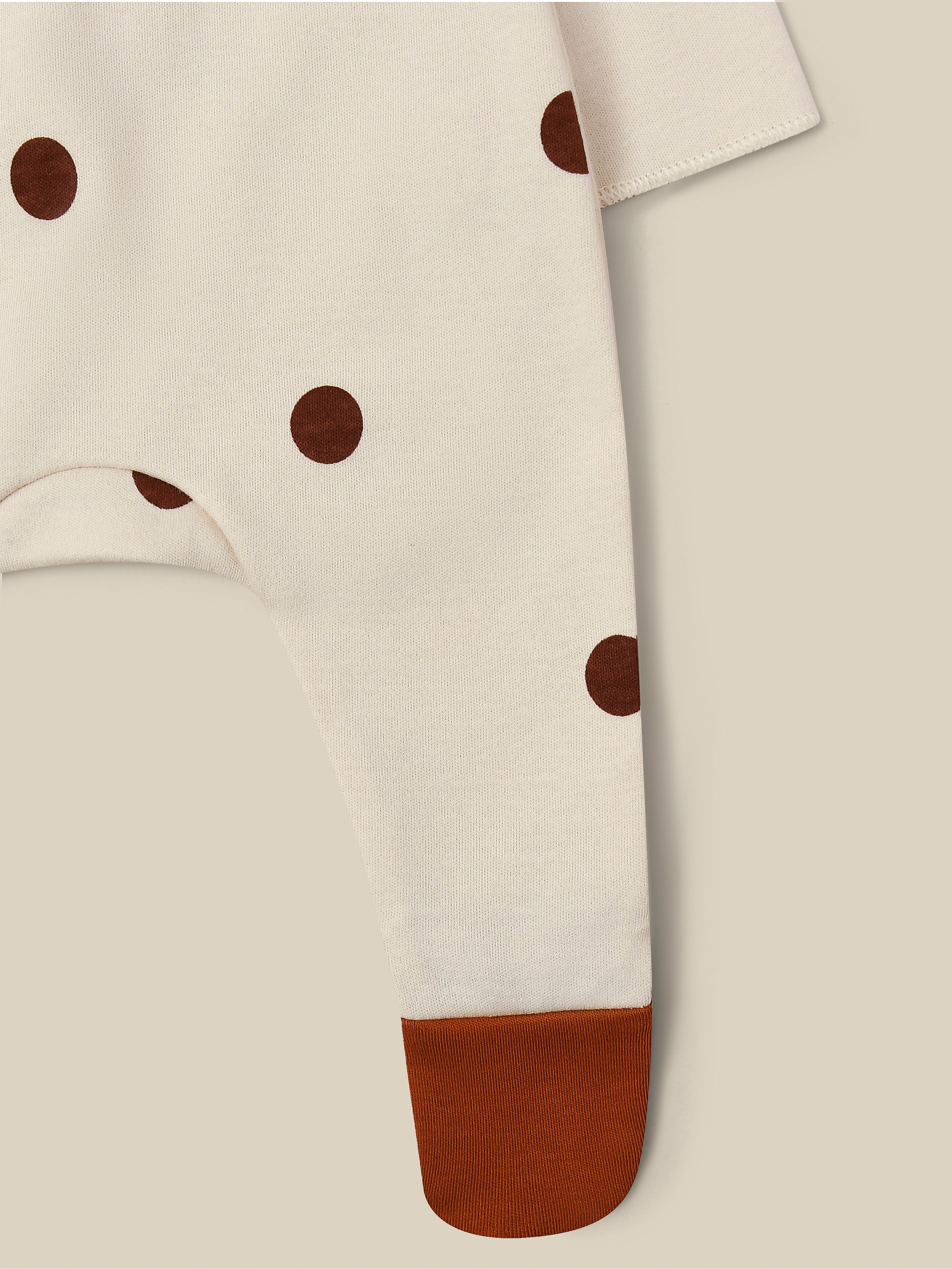 close up of footed suit in cream with through front poppers brown dots & feet