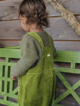 back view of a toddler in boxy green wool jumper & pea pod cotton cord dungarees standing on a green bench