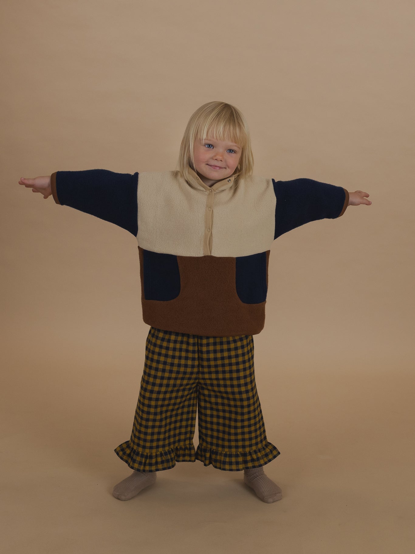 toddler in navy and yellow gingham frill culottes and colour block sweater, standing with arms apart