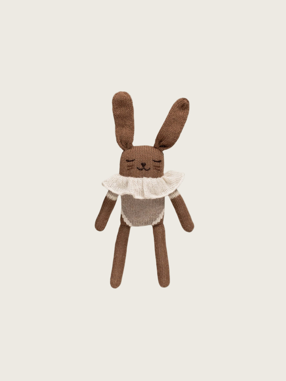 Knitted brown bunny toy with a white ruffled shirt on a light gray background