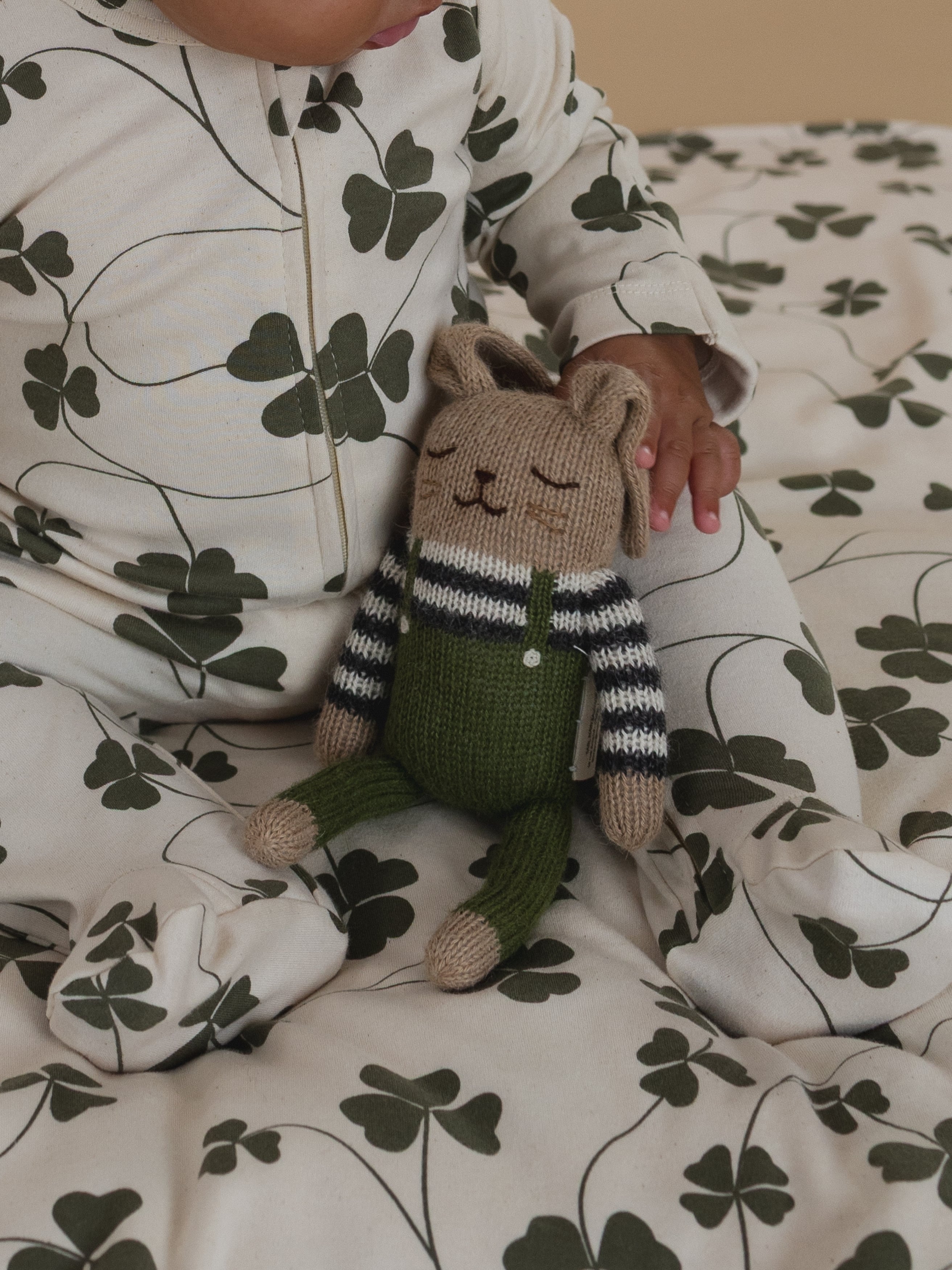 baby in clover print sleepsuit with wool bunny toy in olive overalls with striped top on lap