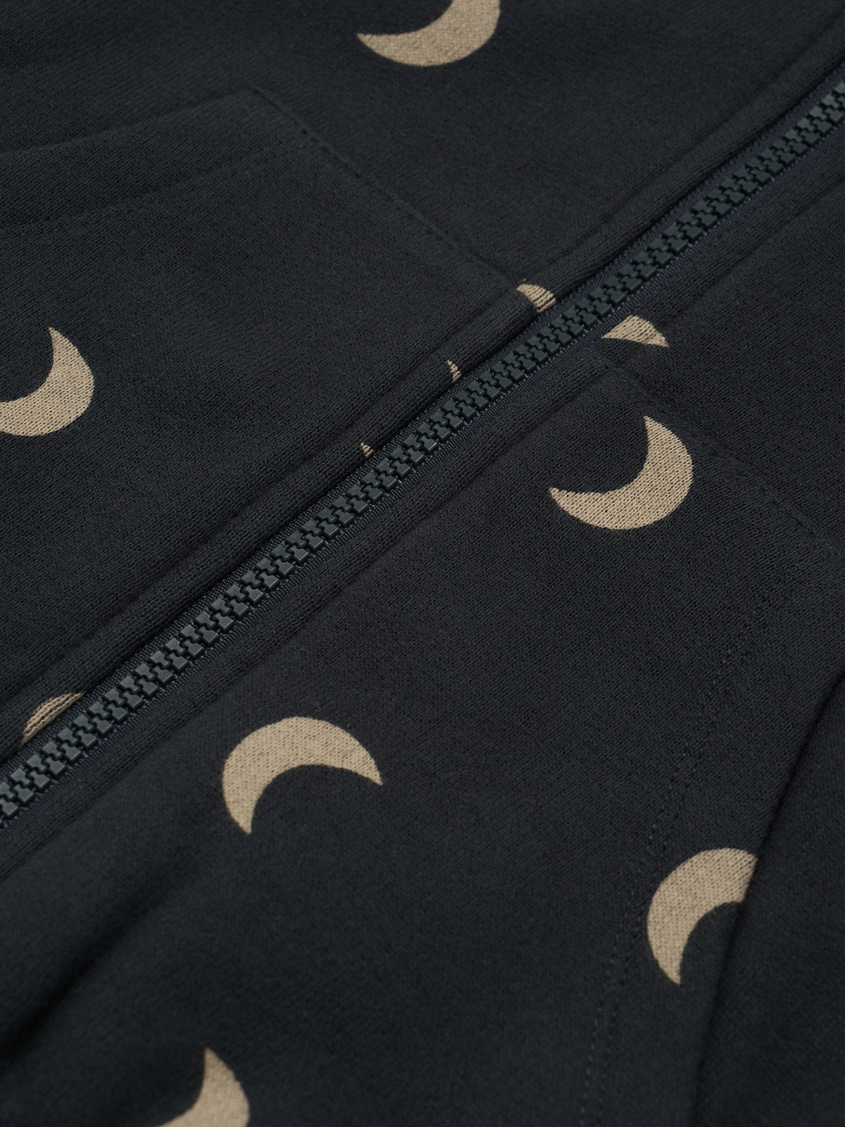 Close-up of a dark navy or black fabric with a repeating beige crescent moon pattern and a matching zipper running diagonally across the frame.