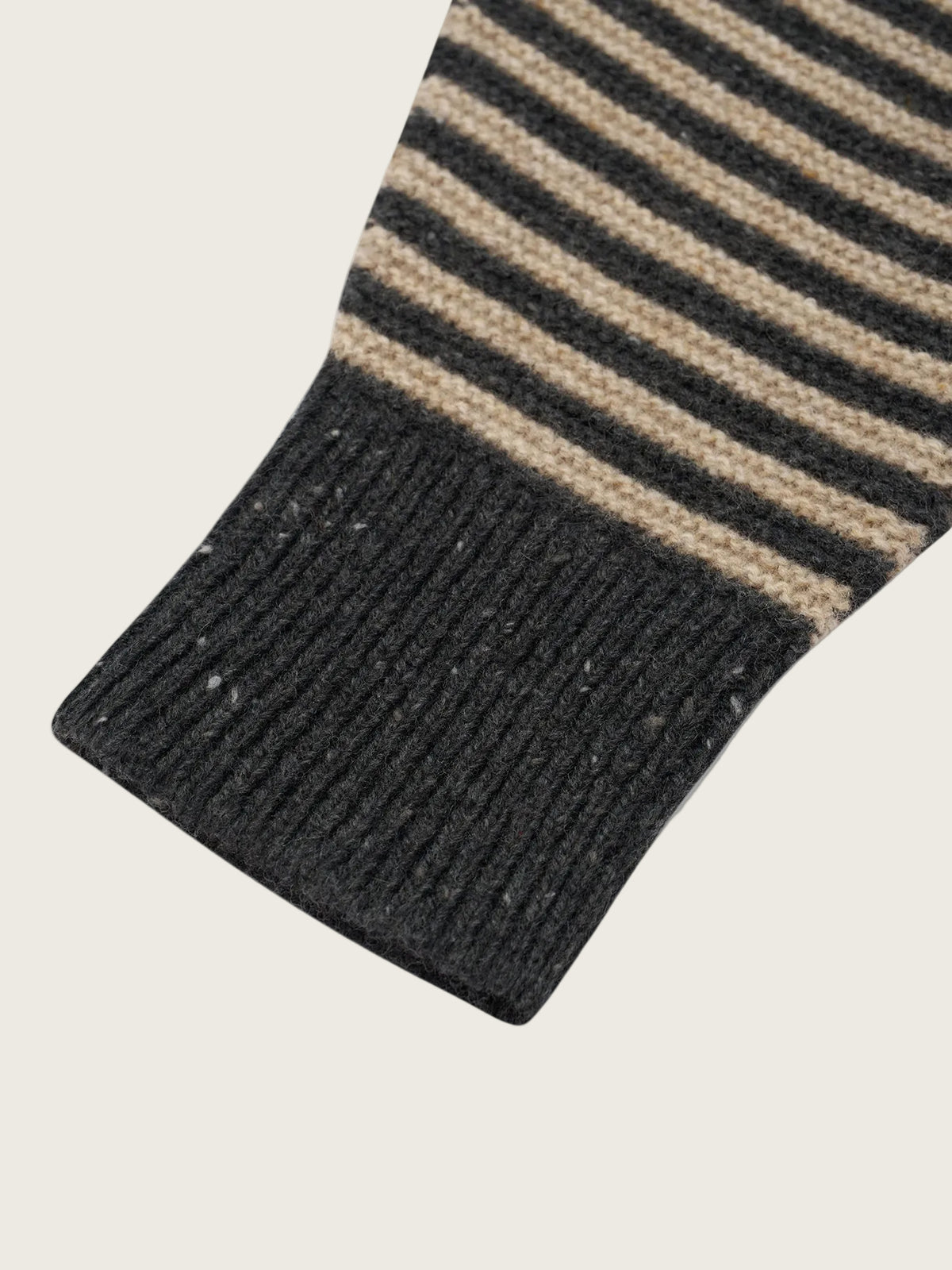 Close-up of a striped knit sock or sleeve cuff in dark charcoal gray and beige, with a ribbed knit cuff on a white background.