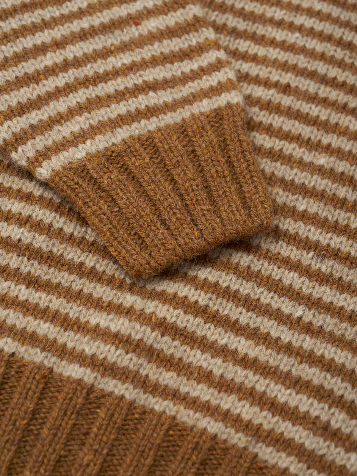 Close-up of a striped knit garment, showing alternating warm brown and cream horizontal stripes with a ribbed brown cuff.