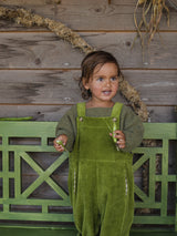 child wearing boxy artichoke green wool jumper & pea pod green cotton cord dungarees holding pea pods