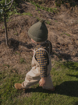 child in yellow & navy gingham flannel shirt & beige dungarees & green beanie walking in garden