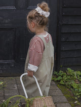 back view of child in red stripes sweatshirt with grey oversized dungarees pulling rattan trolley with vegetables