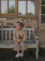 child in terry cotton brown sweatshirt with pear gingham culottes with frills & wool ballet flats sitting on bench