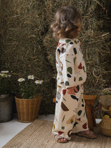 child in wide leg pants & sweatshirt with fresh farm produce print & sandals in backyard