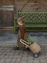 child wearing brown wool cardigan & gingham flannel skirt in navy & yellow pulling rattan trolley with herbs