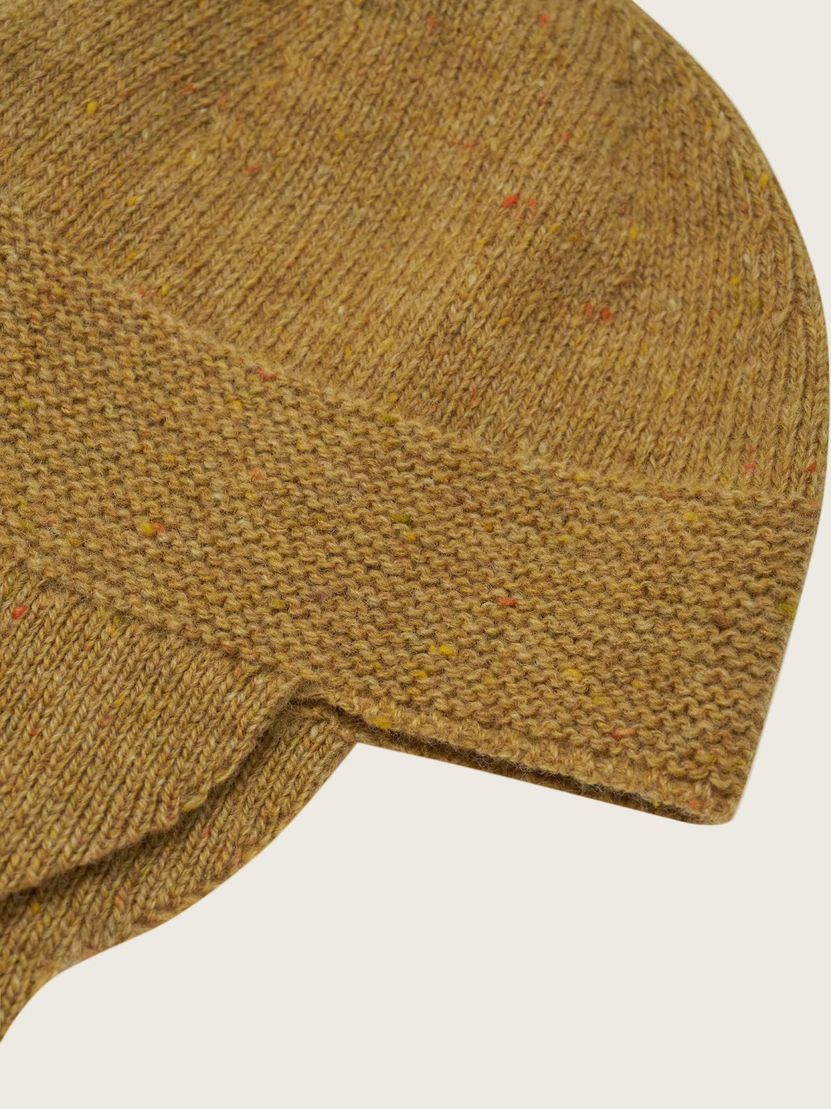 Close-up of a chunky knit beanie hat in a warm camel brown color with subtle multicolored flecks, shown on a plain white background.