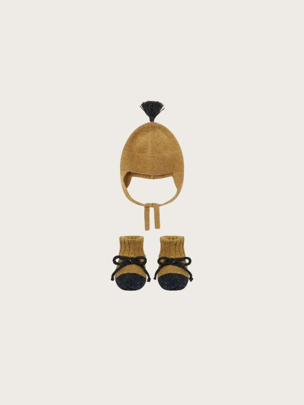 A baby winter hat and bootie set in a warm camel/tan color with black accents, including a small black pom-pom on the hat and black toe caps on the knit booties, shown on a plain white background.