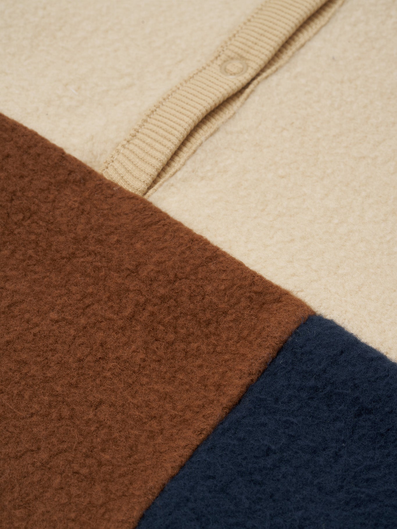 close up of organic fleece colour block cream sweater with brown and navy details, and front poppers