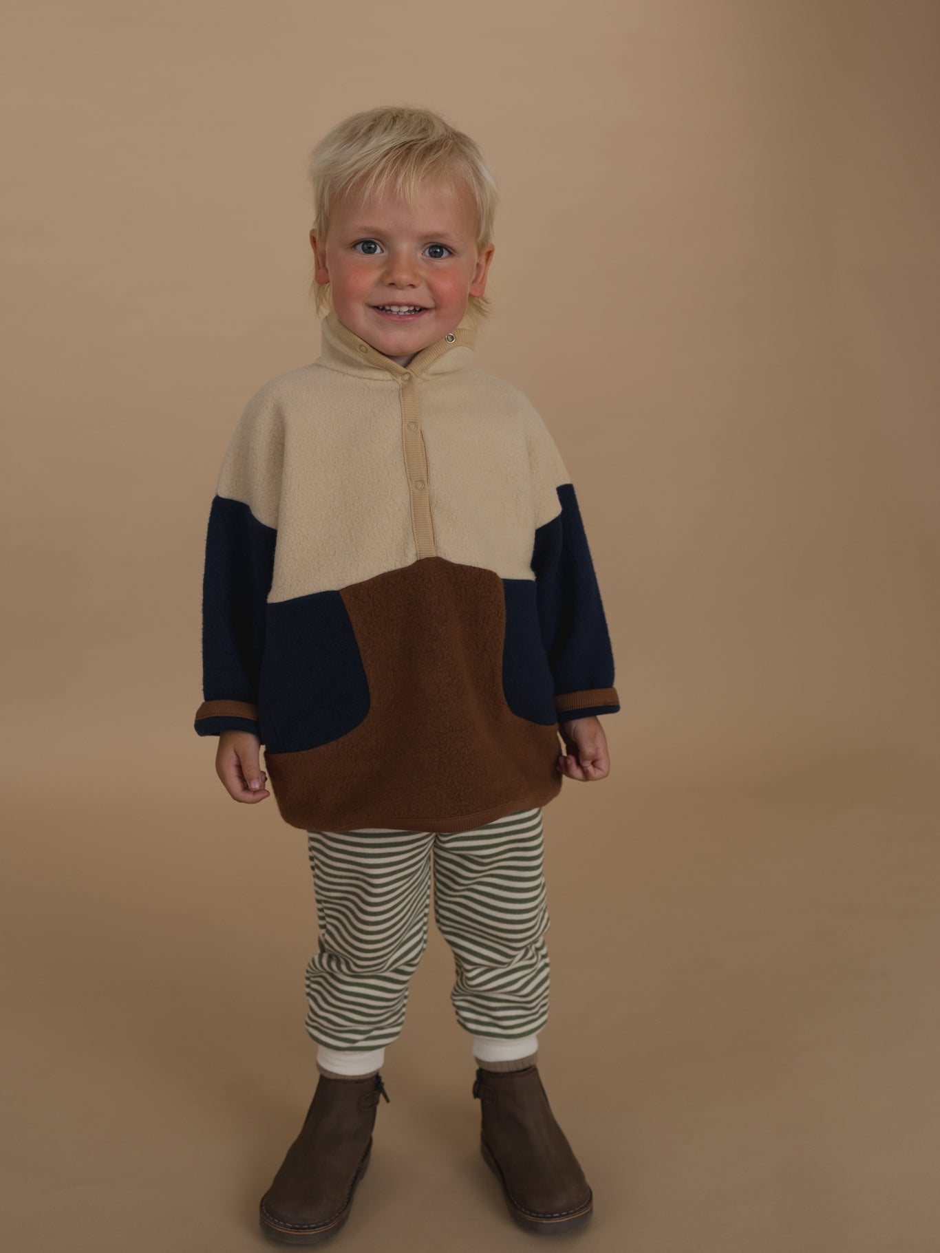 toddler wearing cream, navy and brown colour block fleece sweater with striped pants and boots