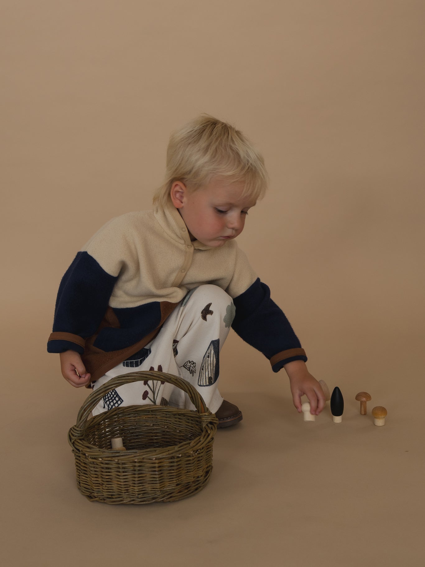 toddler in cream, navy and brown colour block fleece sweater and pants with prints, picking up toys