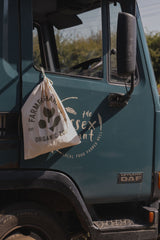 cream organic cotton drawstring bag with green logo & text hanging on door lock knob of farm truck