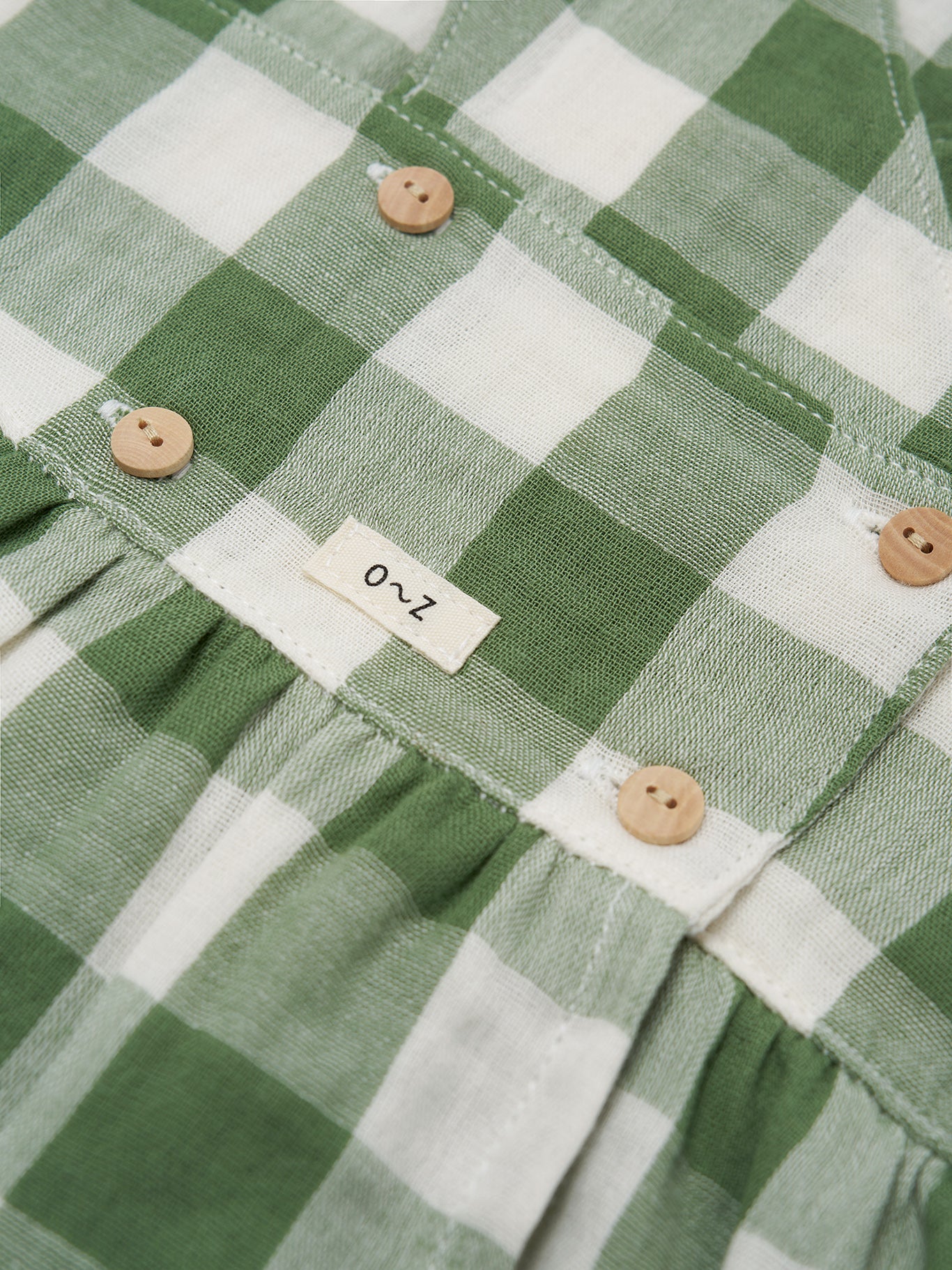Green and white checkered fabric with buttons and a label on a close-up view