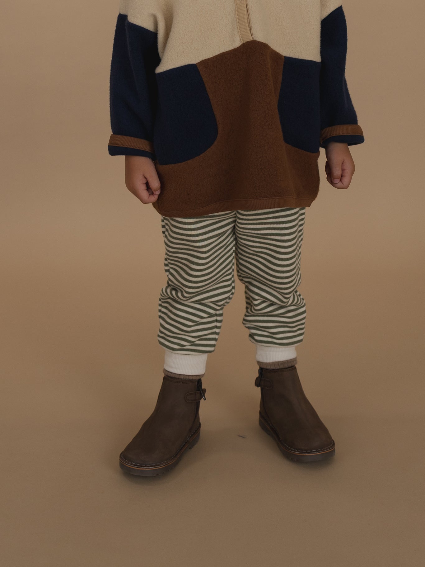 close up of a toddler in fern green and white striped sweatpants, colour block sweater, and boots