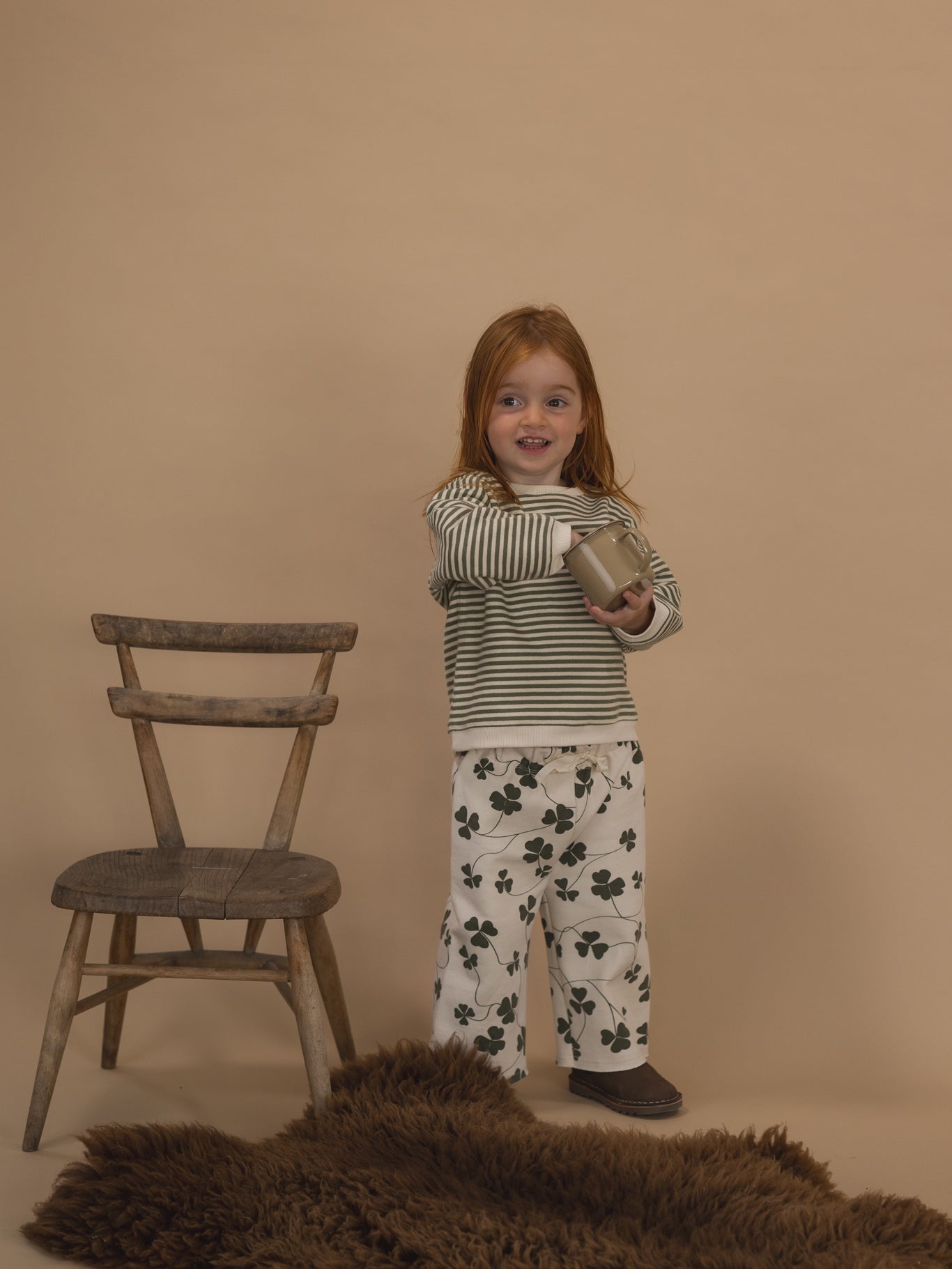 toddler in green and white striped sweatshirt, and wide leg pants with clover print, with hand in a cup
