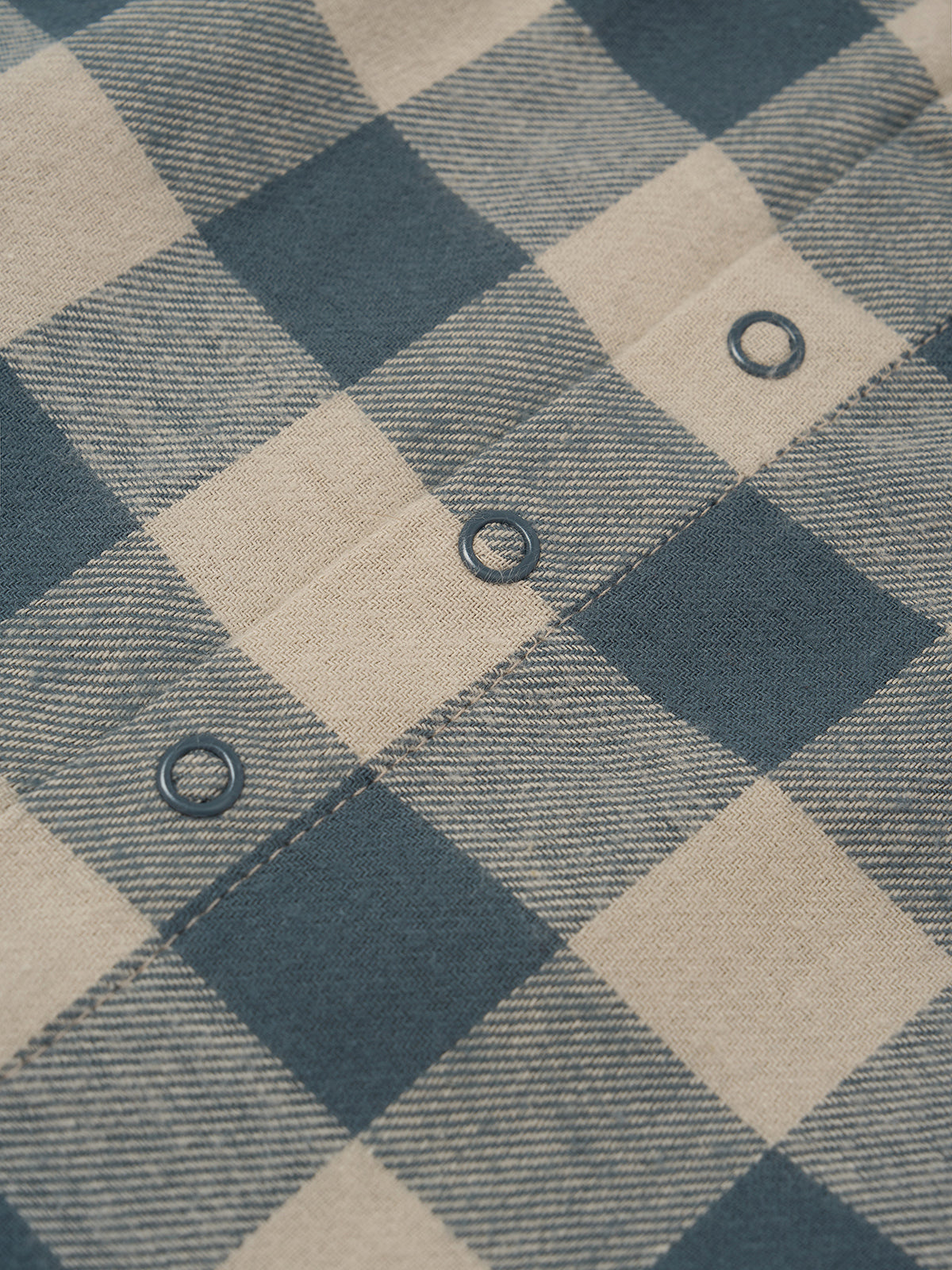Close-up of a blue and beige buffalo plaid fabric with a buttoned pocket showing dark metal snap buttons.