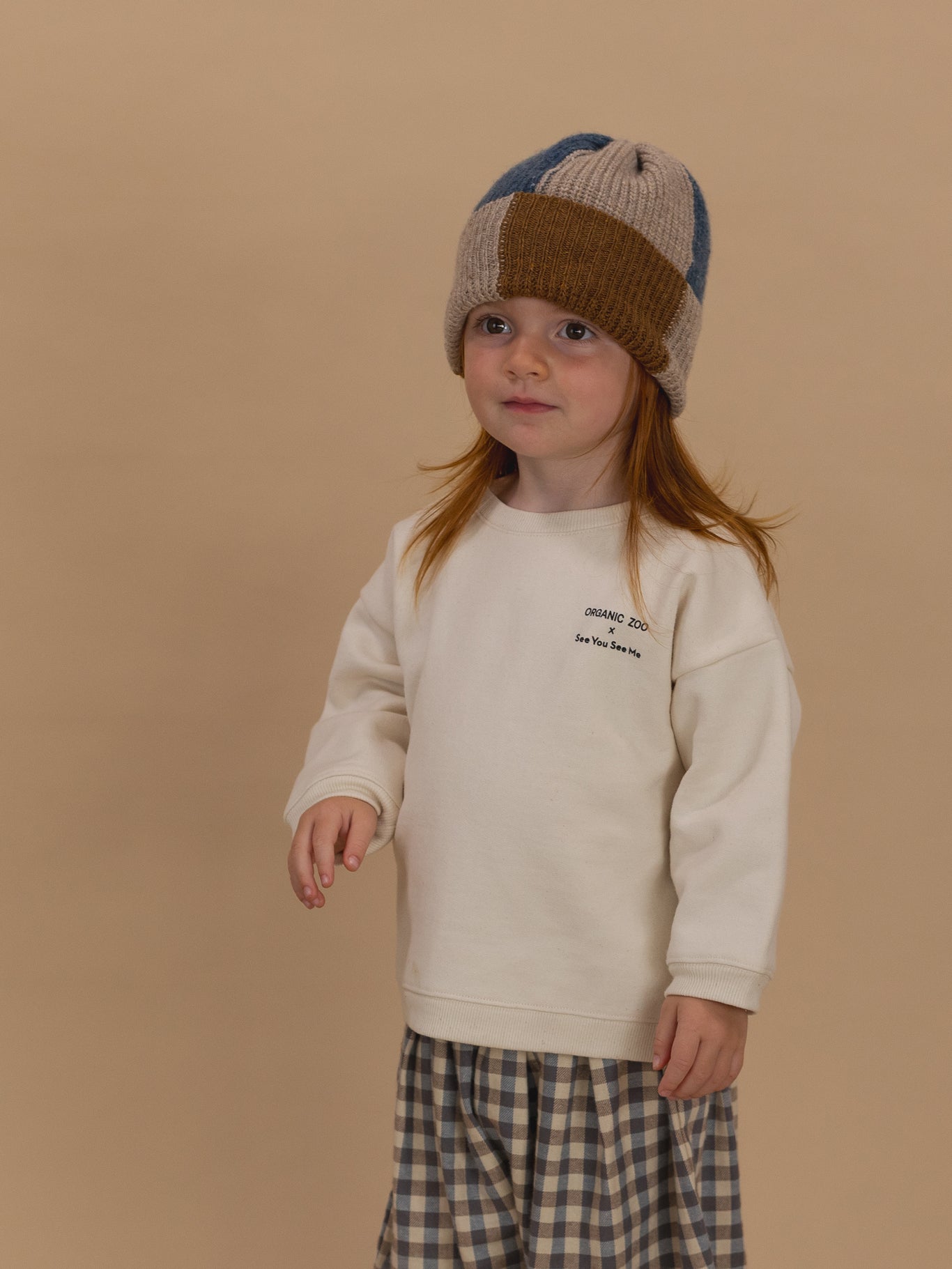 toddler in sweatshirt with ORGANIC ZOO x See You See Me logo with gingham pants and patchwork beanie