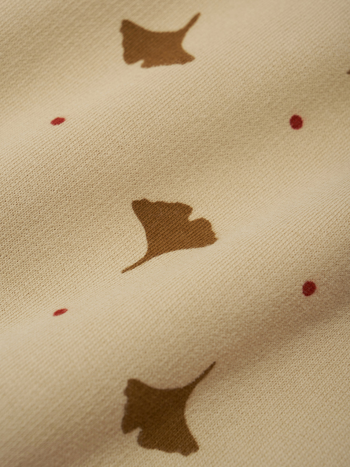 Close-up of a cream-colored fabric with a pattern of brown ginkgo leaves and small red dots.