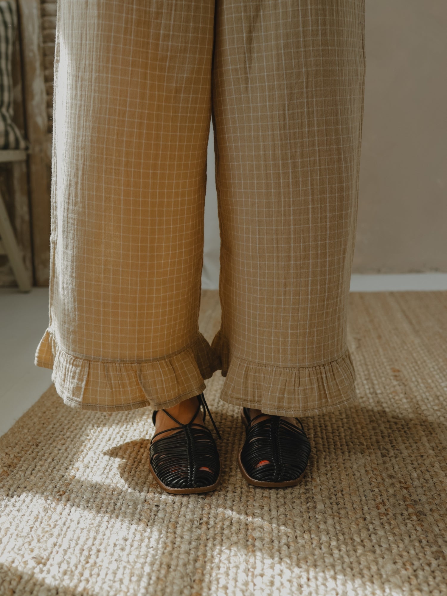 Person wearing beige checkered pants and black sandals on a textured floor.