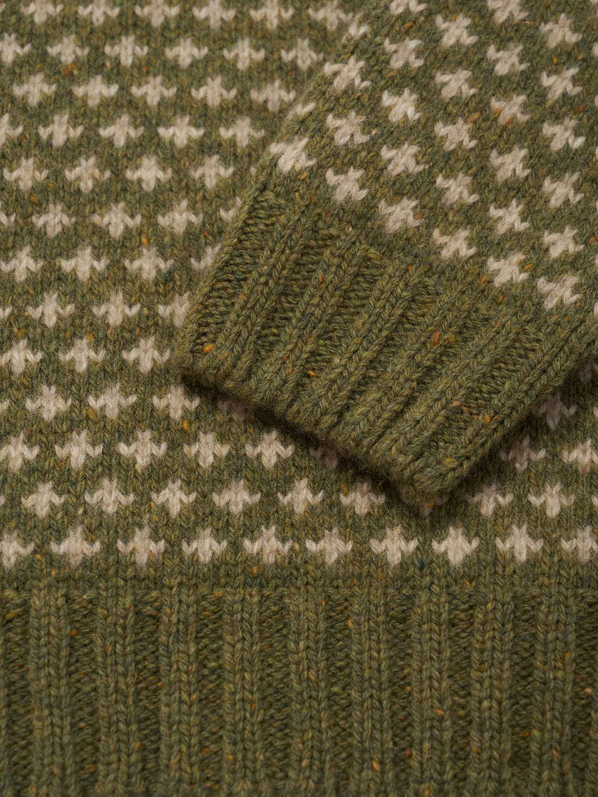 Close-up of a knitted sweater showing an olive green and cream fair isle pattern with ribbed knit details.