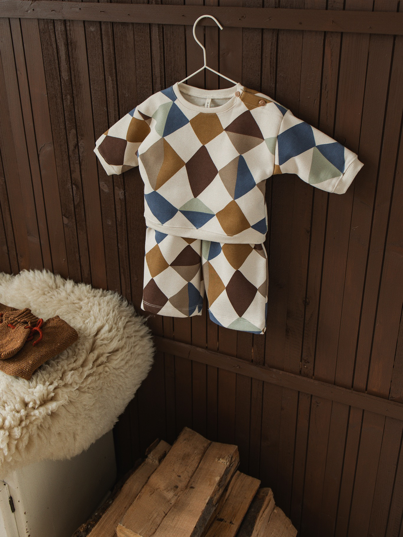 matching baby sweatshirt & pants with multicolour geometric patchwork, hanging on rack