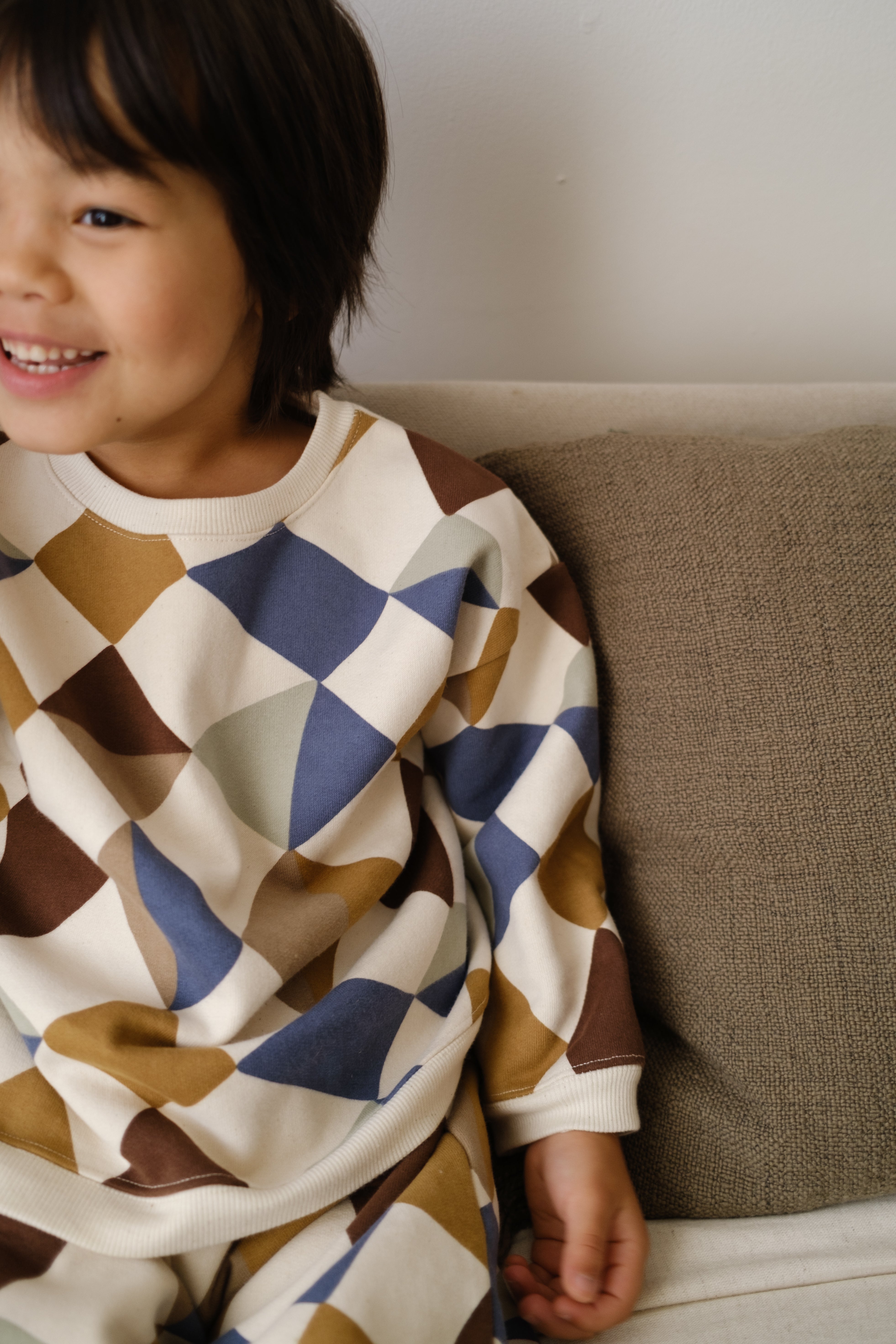 close up of toddler in matching cream sweatshirt & pants with multicolour geometric patchwork print