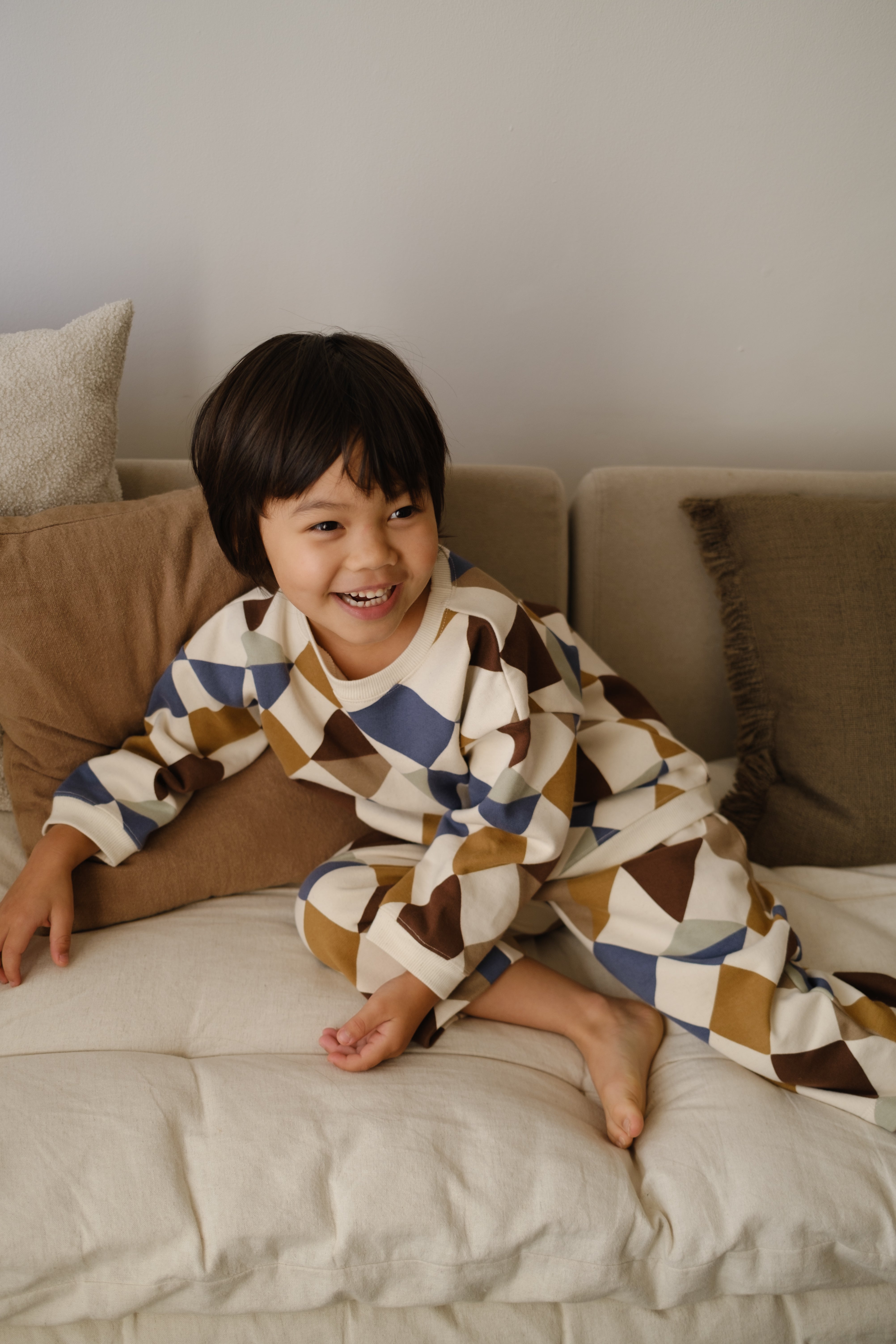 toddler in matching cream sweatshirt & pants with multicolour geometric patchwork, playing on bed