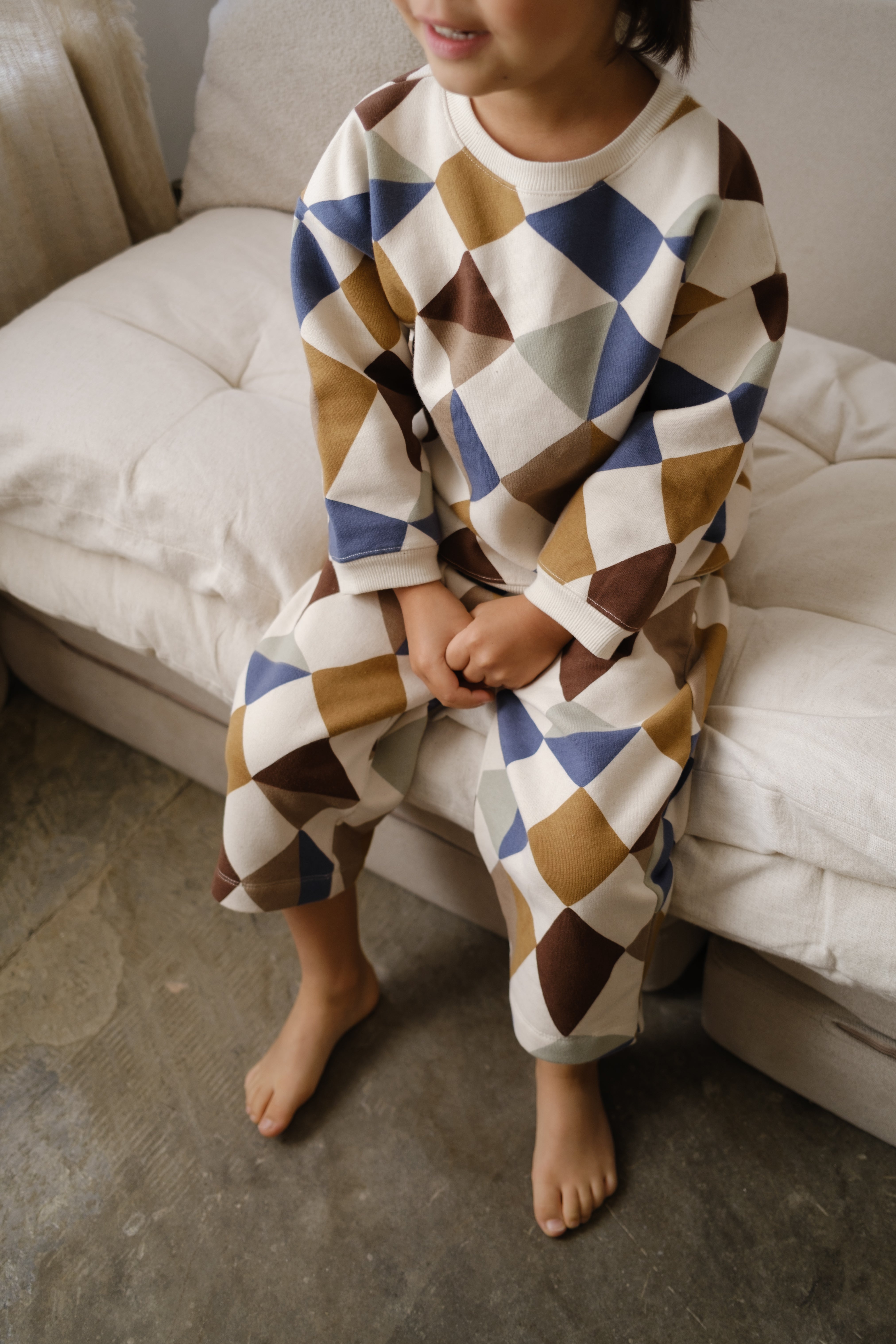 close up of toddler in matching cream pants & sweatshirt with multicolour geometric patchwork print