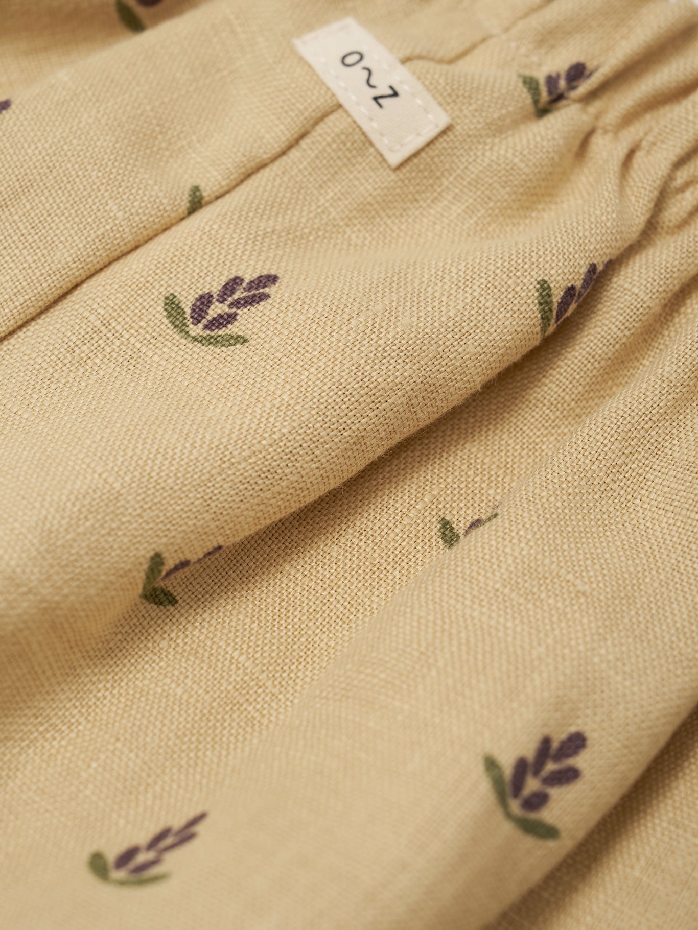 Beige fabric with lavender designs and a label on a beige background