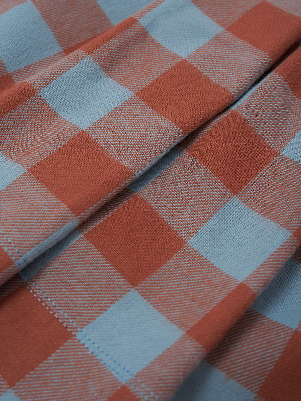 A close-up of a plaid fabric with a checkered pattern in terracotta orange and light blue, showing the woven texture and folded folds.