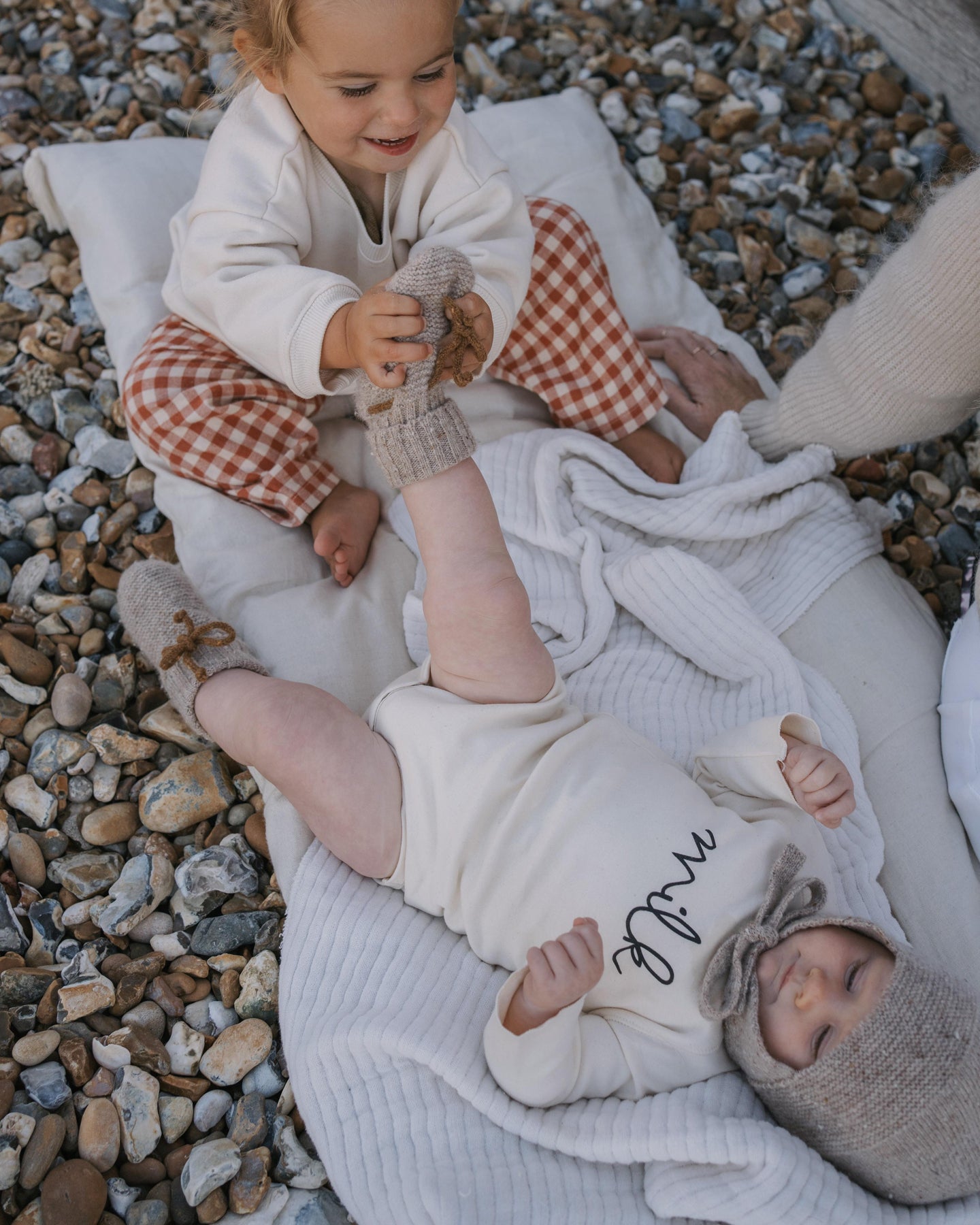 Two children in undyed cotton clothes lying on a blanket on a pebbly surface