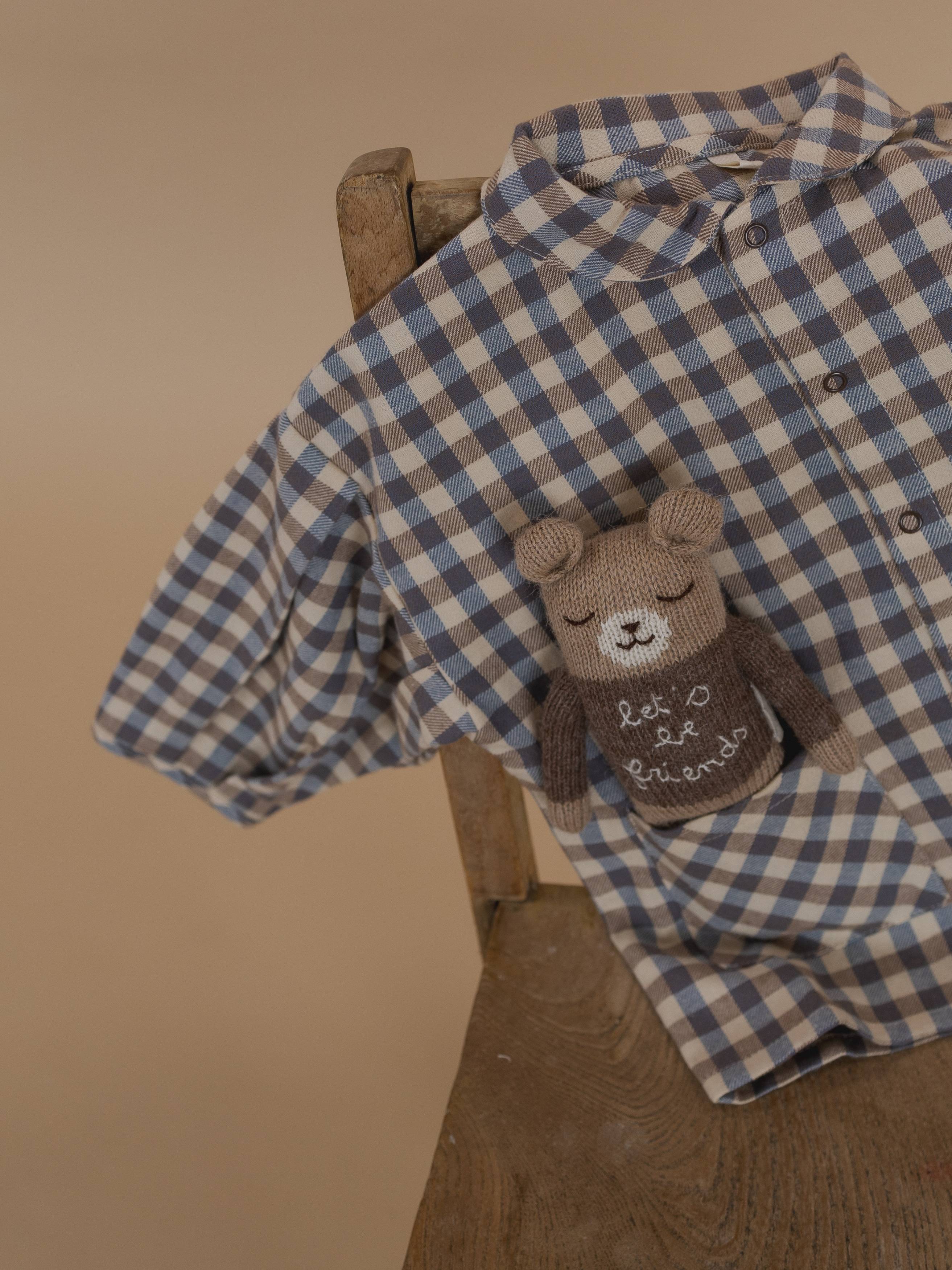 knitted wool teddy cuddly toy in brown jumper with slogan, sitting in a gingham shirt pocket