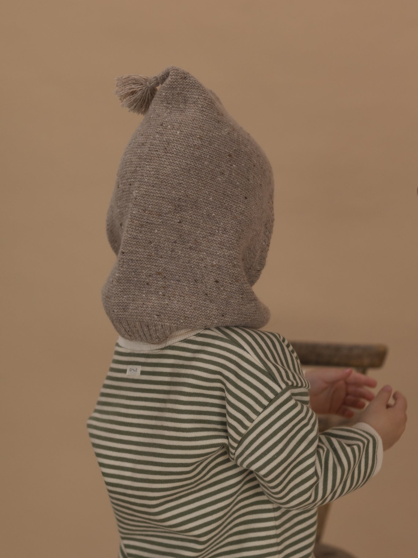 back of a toddler in oatmeal wool knitted balaclava, and fern green striped sweatshirt