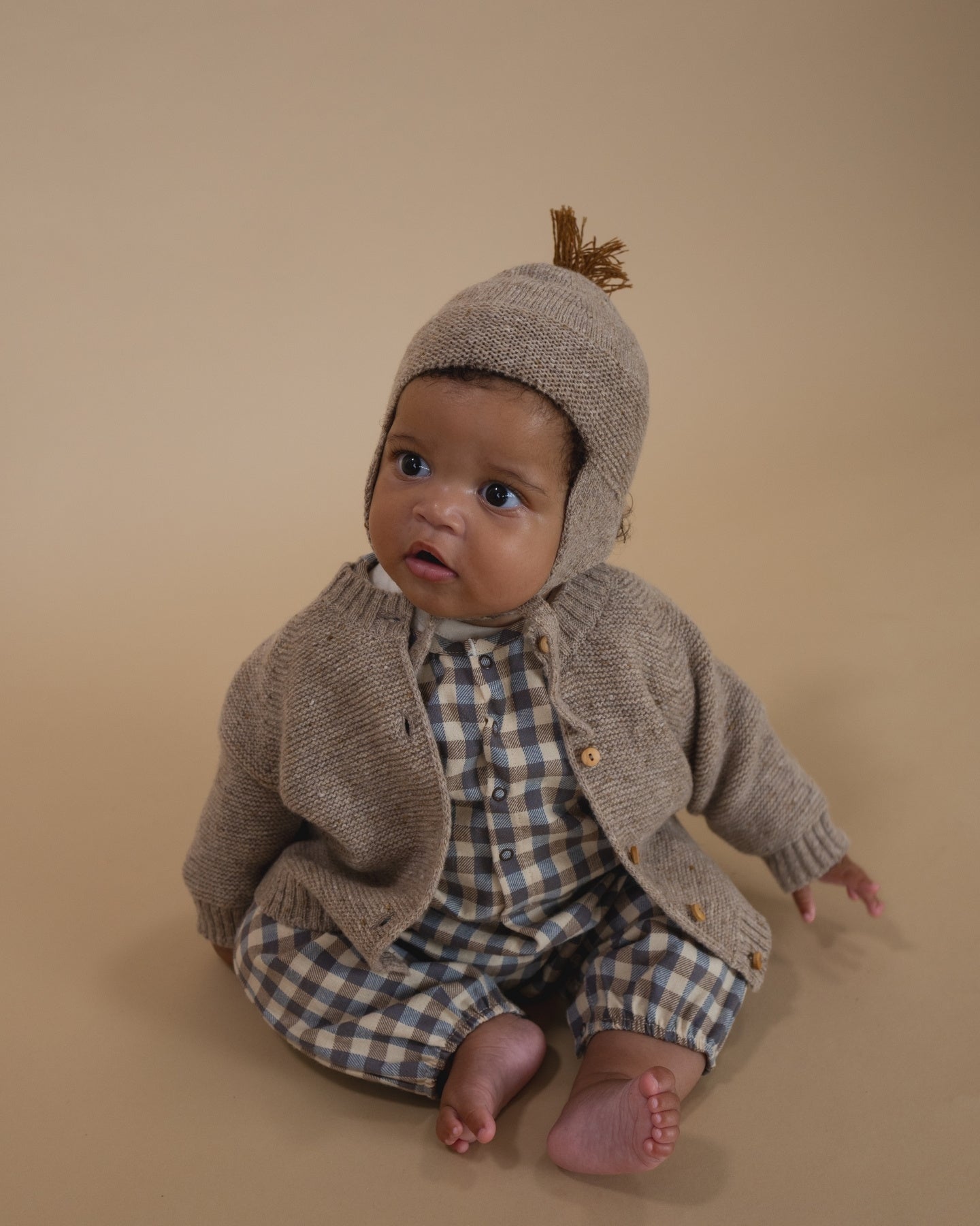 Baby wearing a organic baby outfit with a checkered shirt on a beige background