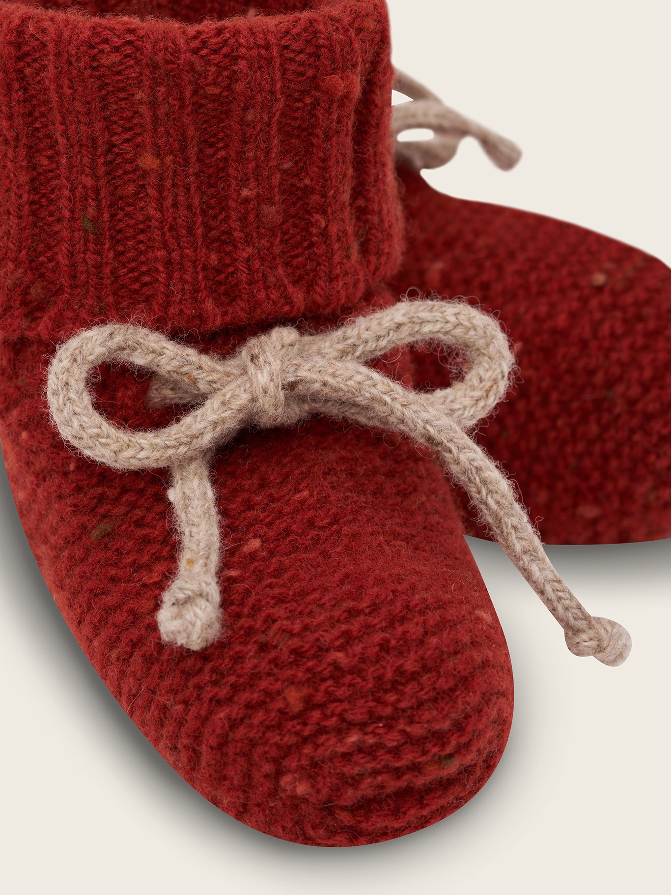 close up of wool booties in paprika red with ribbed cuffs and beige ribbons